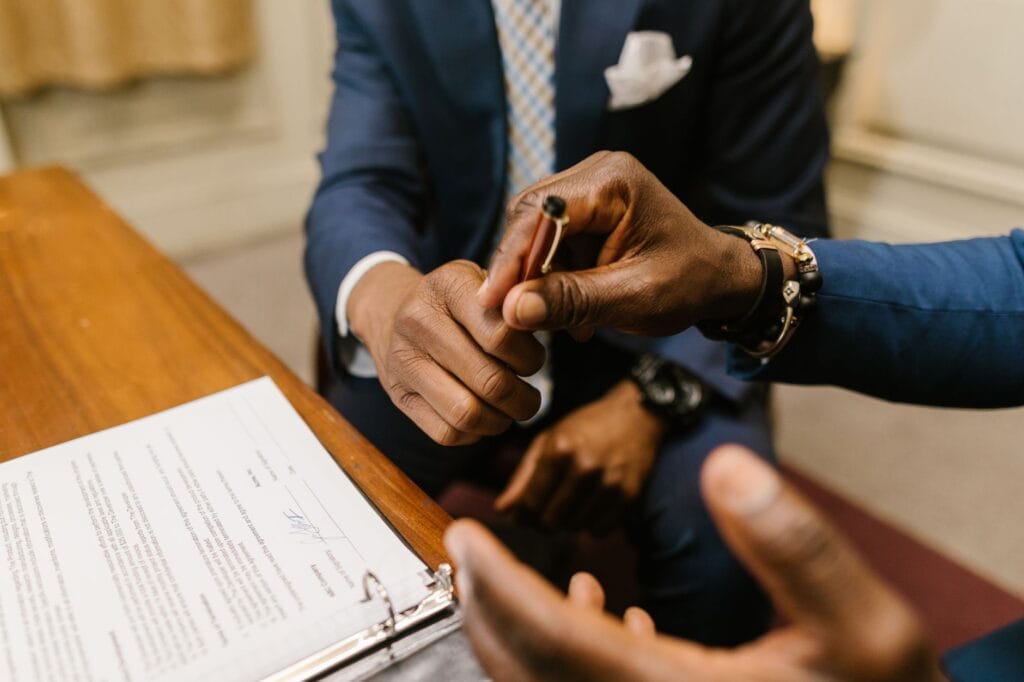 Two businessmen in suits reviewing and finalizing a vendor contract agreement at a desk.