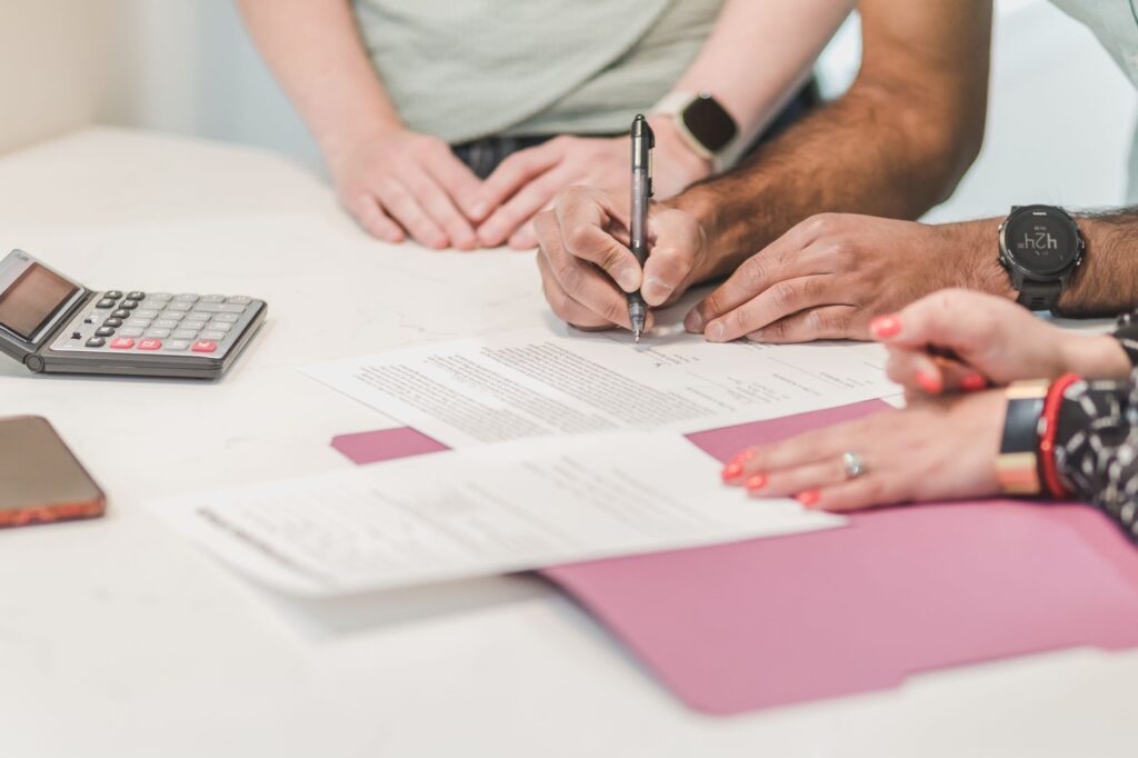 Borrowers signing mortgage refinance loan documents with calculator and paperwork on table