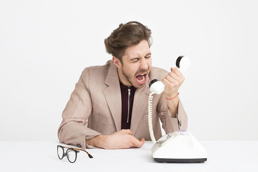 Frustrated man yelling at telephone representing the borrower experience of being bombarded by unsolicited trigger lead calls after a mortgage credit pull