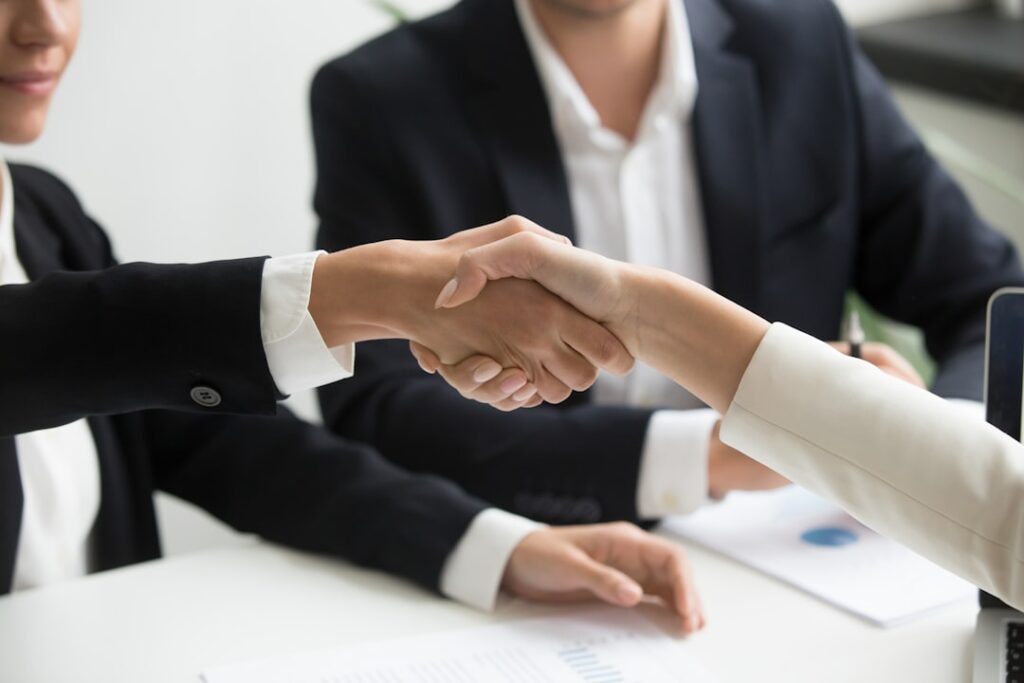 Two professionals shaking hands across a desk representing a loan officer and Realtor referral partnership